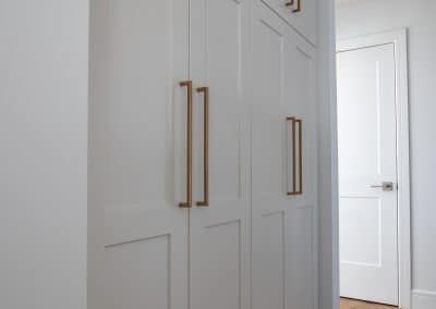A white closet with brass handles in a hallway.