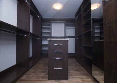 A walk in closet with dark wood cabinets and drawers.
