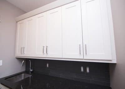 A laundry room with white cabinets and black counter tops.